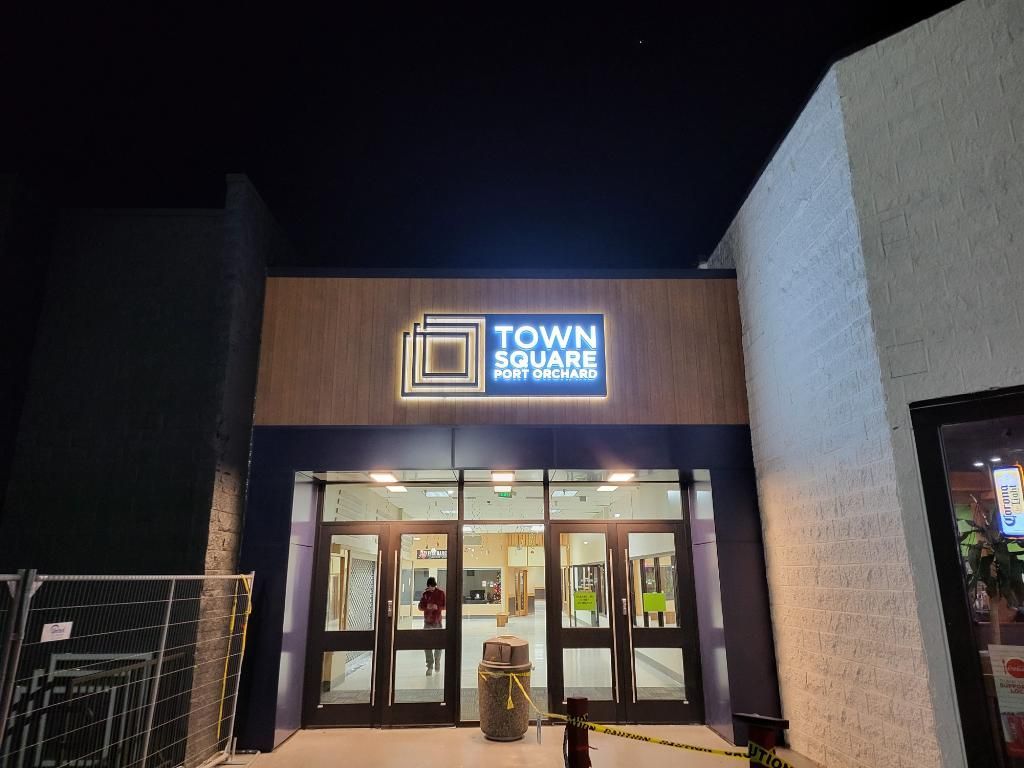 Entrance to town square with lit sign above glass doors.