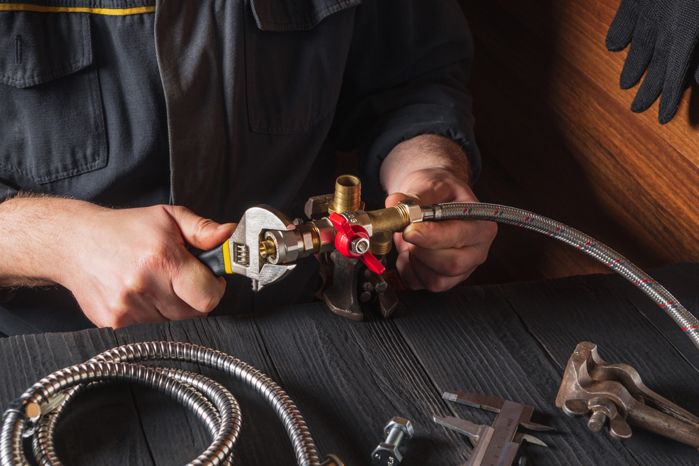 A man is fixing a faucet with a wrench and hose.