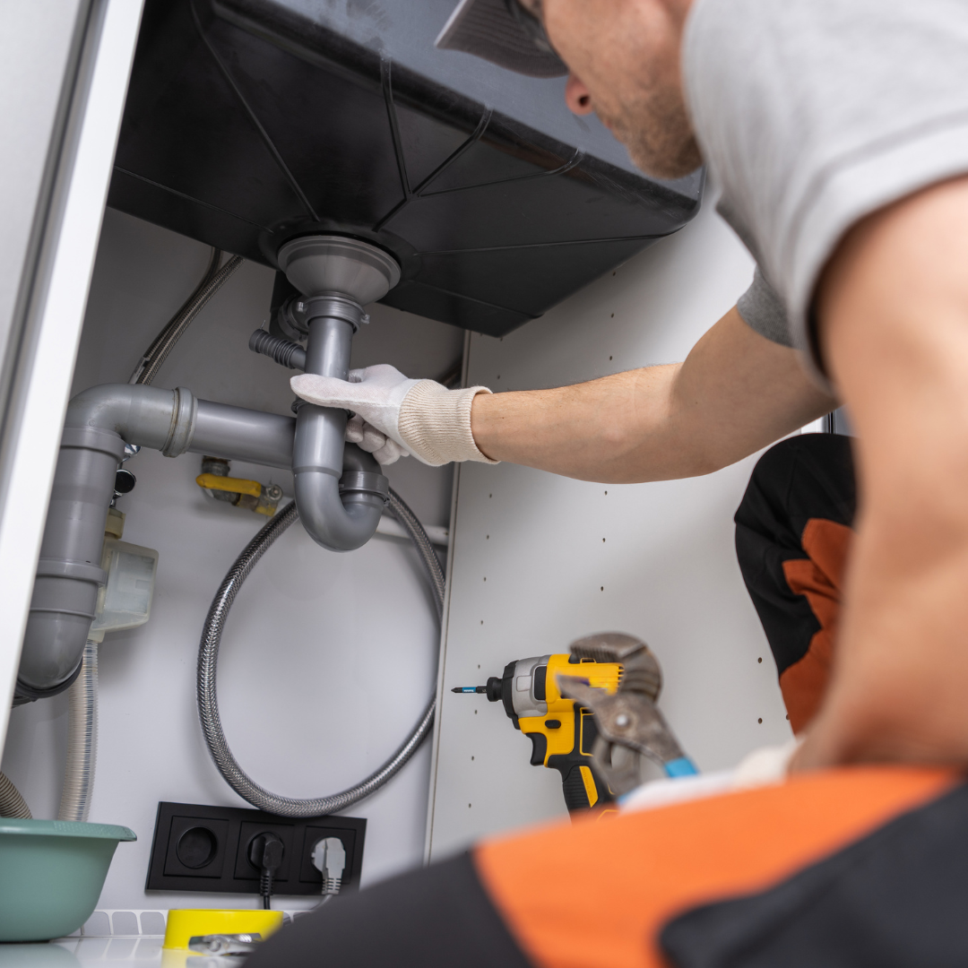 A man is fixing a sink with a drill