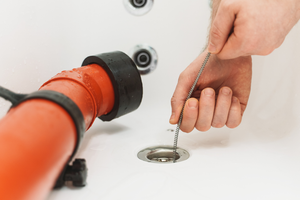 A person is cleaning a drain in a bathtub with a chain.