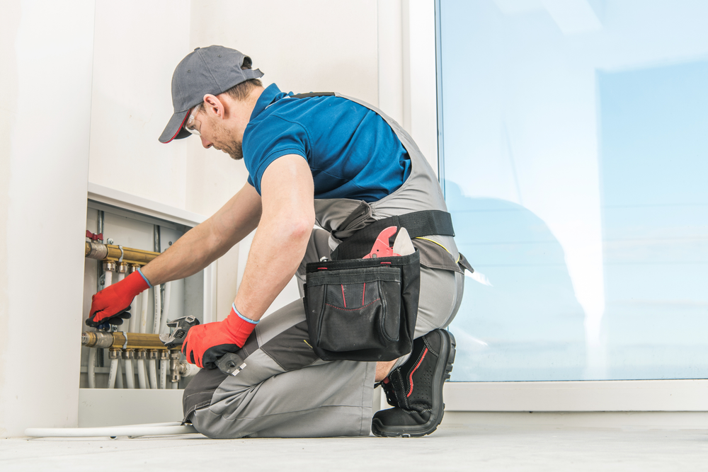 A man is kneeling on the floor working on a pipe.