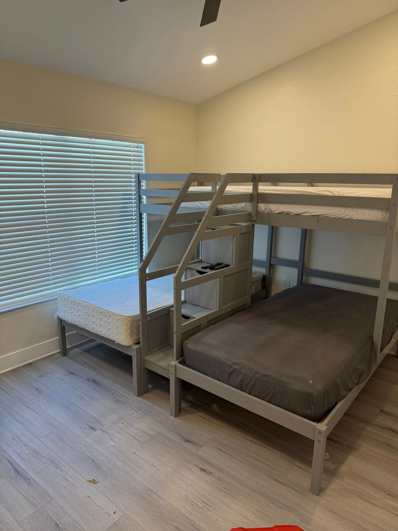 Gray bunk bed with a twin-over-full configuration in a room with a window and wood-look flooring.