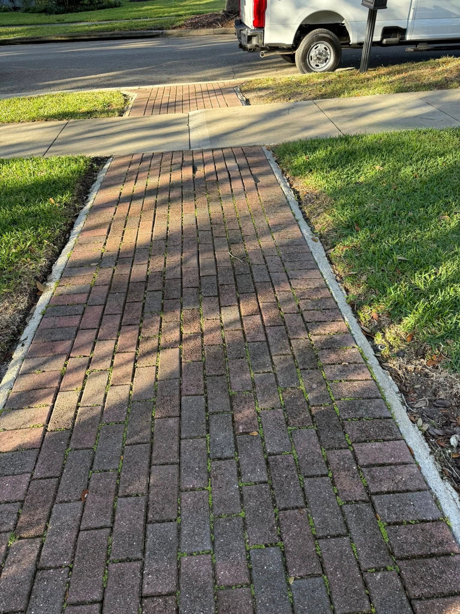 Brick pathway with grass on either side, leading to a street with a white truck.