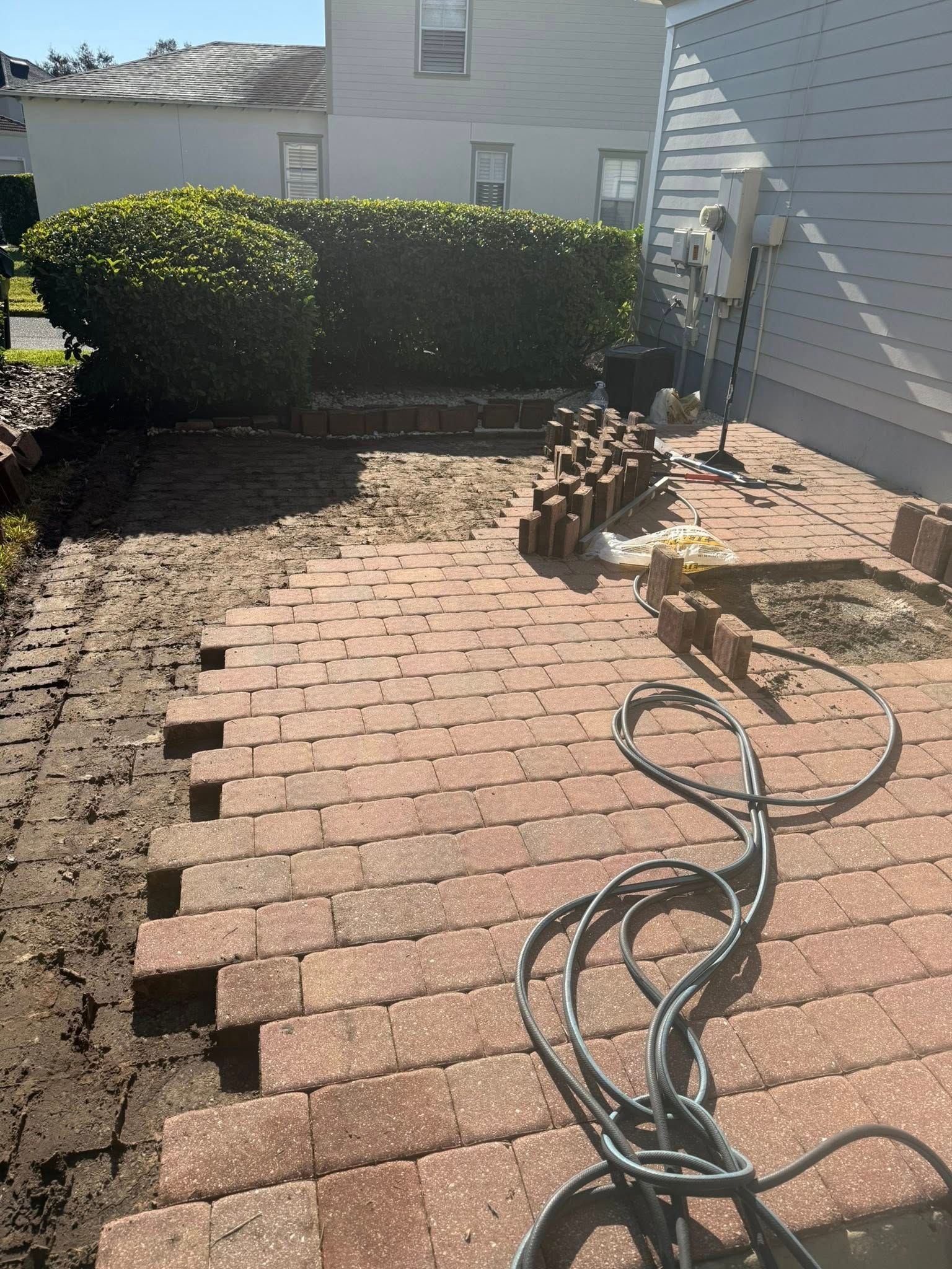 Red brick patio being repaired; bricks removed, soil exposed, power cable visible.