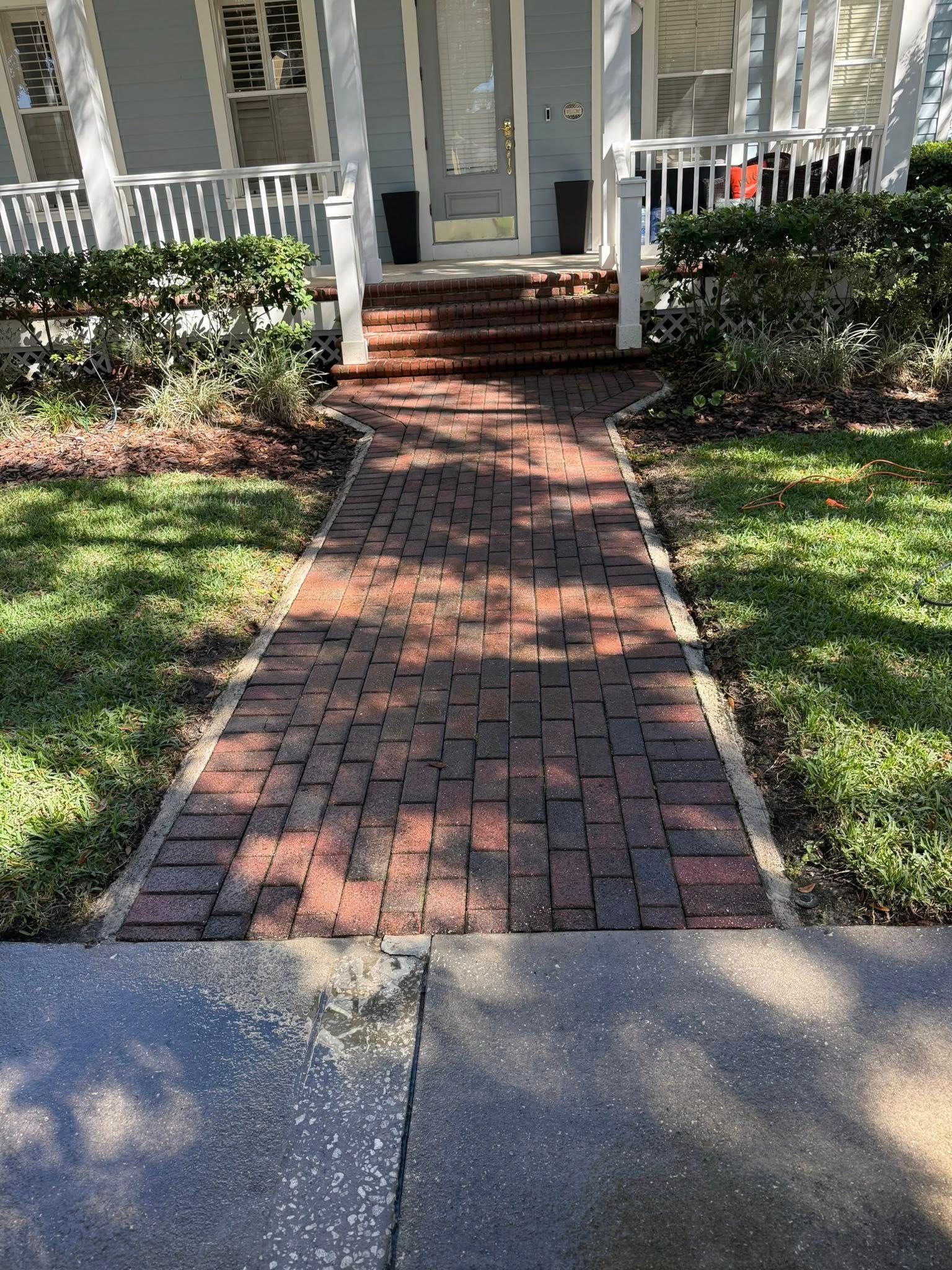 Brick path leads to steps and a light blue house with white trim.
