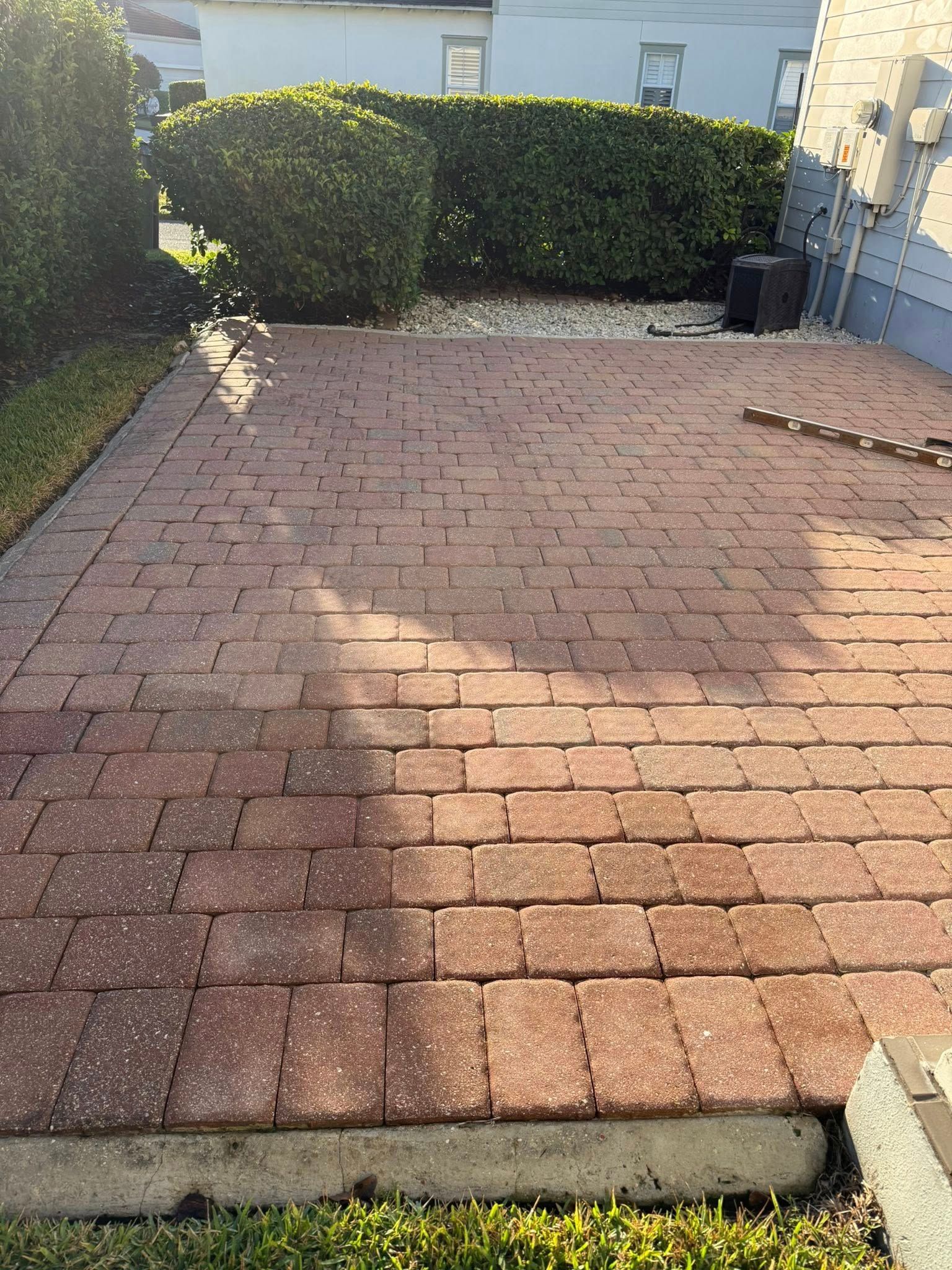 Brick patio in yard with small bushes and a building.