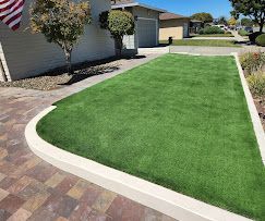 Round stone patio with umbrella, table, and chairs. Lawn and trees in background.