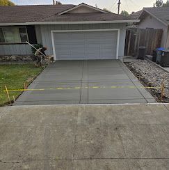 Sidewalk with green grass on either side, street with cars, and houses in the background.