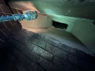 Inside view of a brick chimney with spray-on insulation, a small vent, and a cleaning tool.