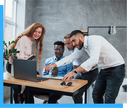 Four people gathered around a laptop, pointing and smiling in an office setting.