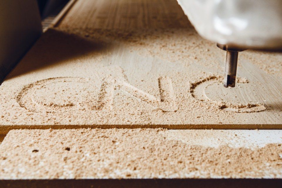 A machine is carving the word cnc into a piece of wood.