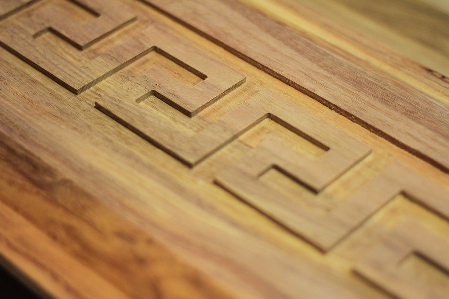 A close up of a piece of wood with a greek key pattern carved into it.