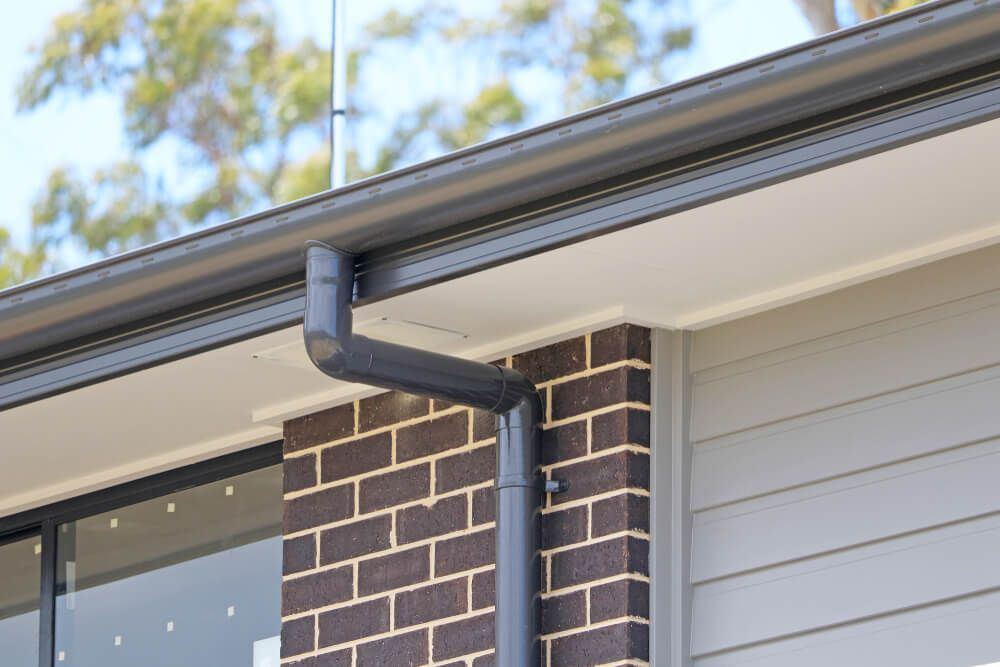 Dark Grey Gutters and Downspout on A Brick and Siding Exterior of A Building — All-Clear Gutter Guard NQ in Earlville, QLD