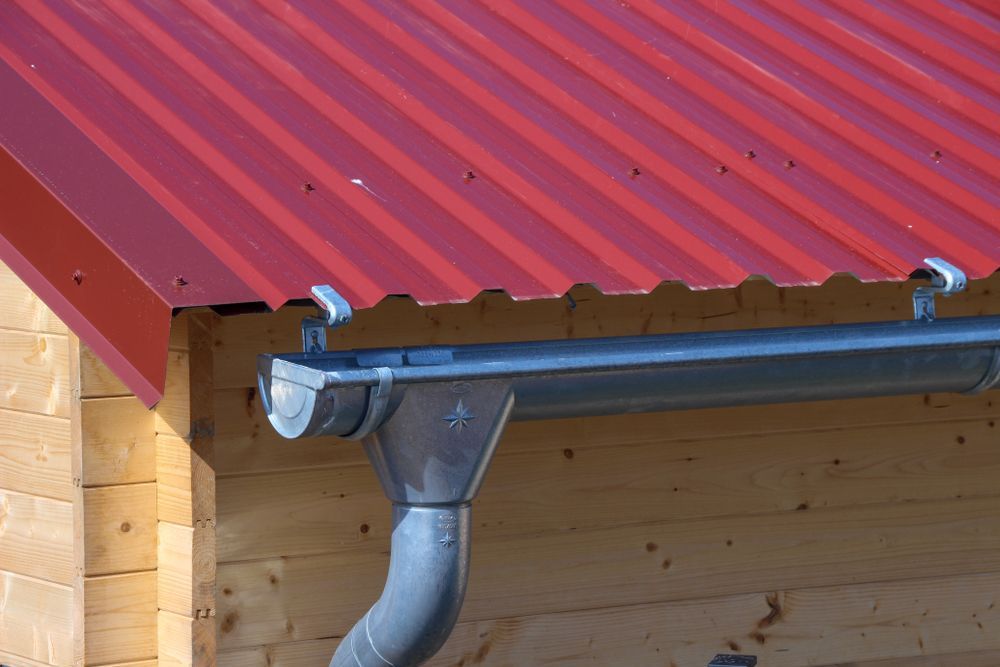 Red corrugated metal roof with silver rain gutter and downspout on a wooden building — All-Clear Gutter Guard NQ in Cairns City, QLD