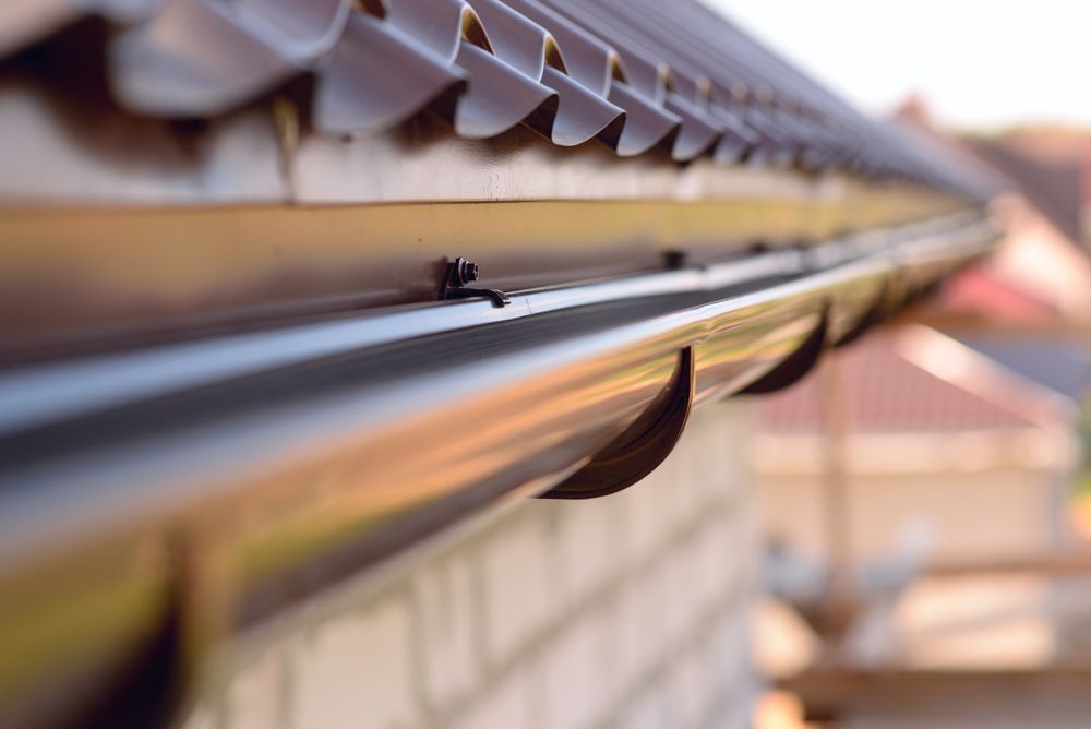 Brown rain gutter on a roof, close-up with a brick wall below — All-Clear Gutter Guard NQ in Kuranda, QLD