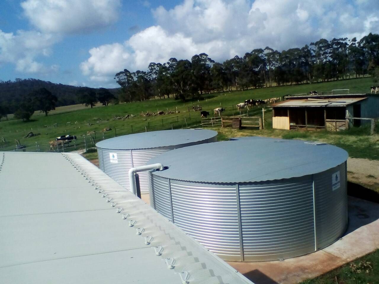 Two Large, Corrugated Metal Water Storage Tanks on A Rural Property with A Green Field and Trees in The Background — All-Clear Gutter Guard NQ in Atherton, QLD