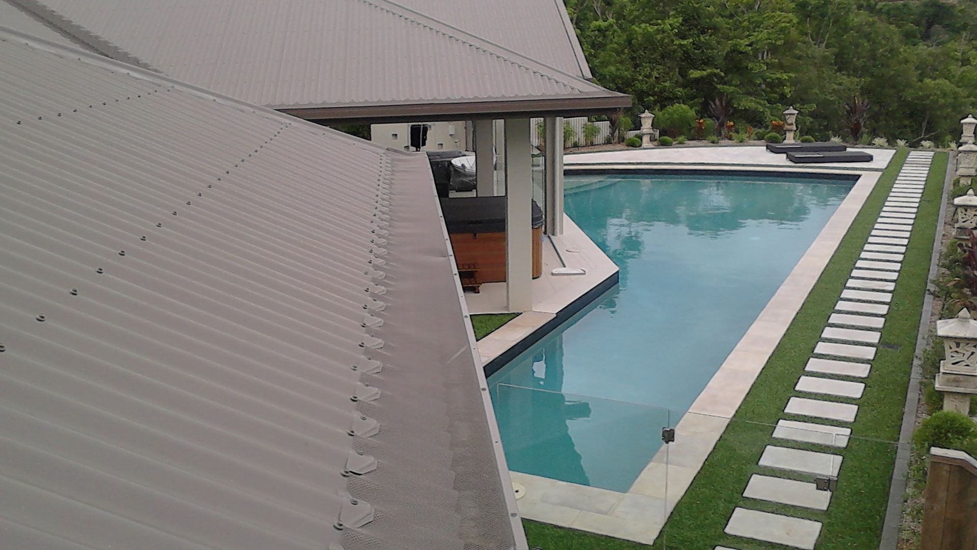 Grey Roof Overlooking a Swimming Pool, Patio, and Stone Path, Surrounded by Greenery — All-Clear Gutter Guard NQ in Trinity Beach, QLD