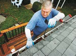 A Man Is Cleaning A Gutter On The Roof Of A House — All-Clear Gutter Guard NQ in Cairns, QLD