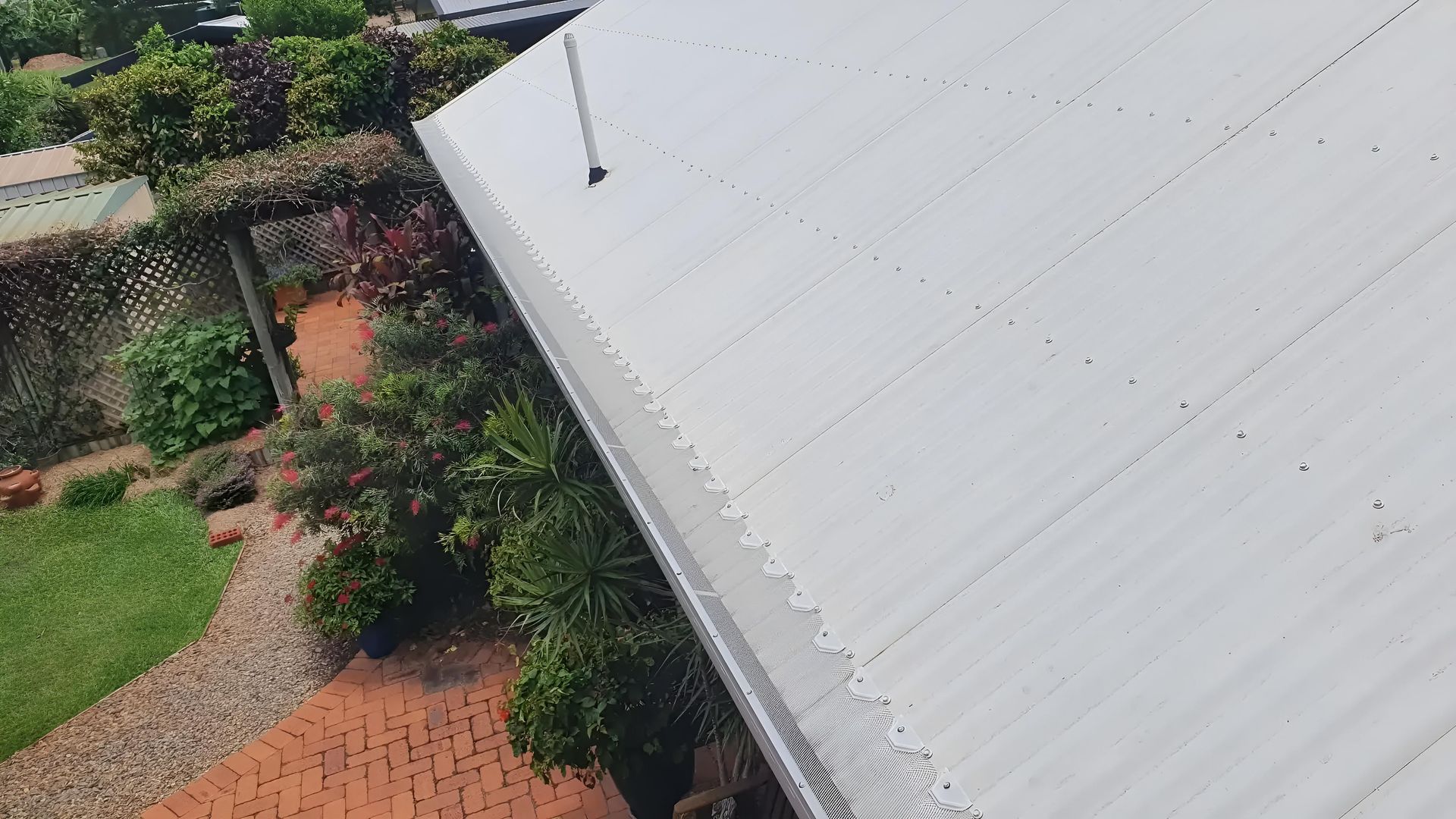 White Corrugated Roof Edge with Gutter, Overlooking a Garden with Brick Pathway and Green Foliage — All-Clear Gutter Guard NQ in Yungaburra, QLD
