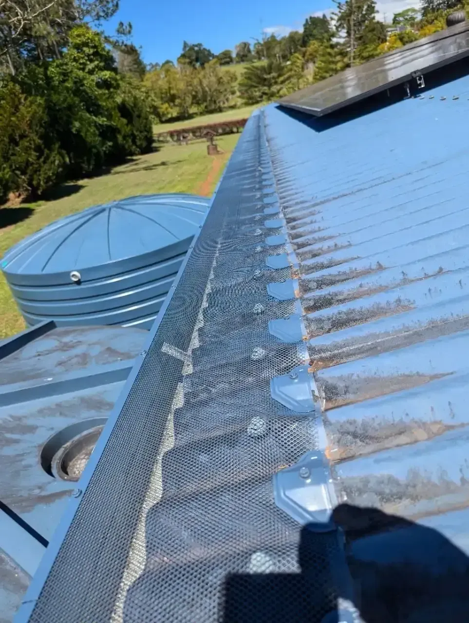 A Person is Cleaning a Gutter on a Blue Roof — All-Clear Gutter Guard NQ in Palm Cove, QLD