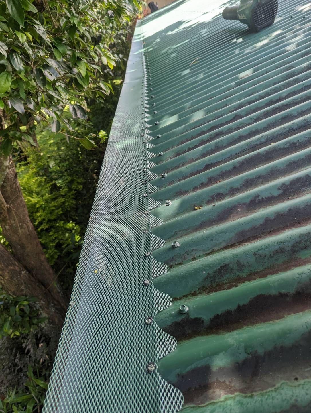 A green gutter with a mesh on it is sitting on top of a green roof — All-Clear Gutter Guard NQ in Palm Cove, QLD