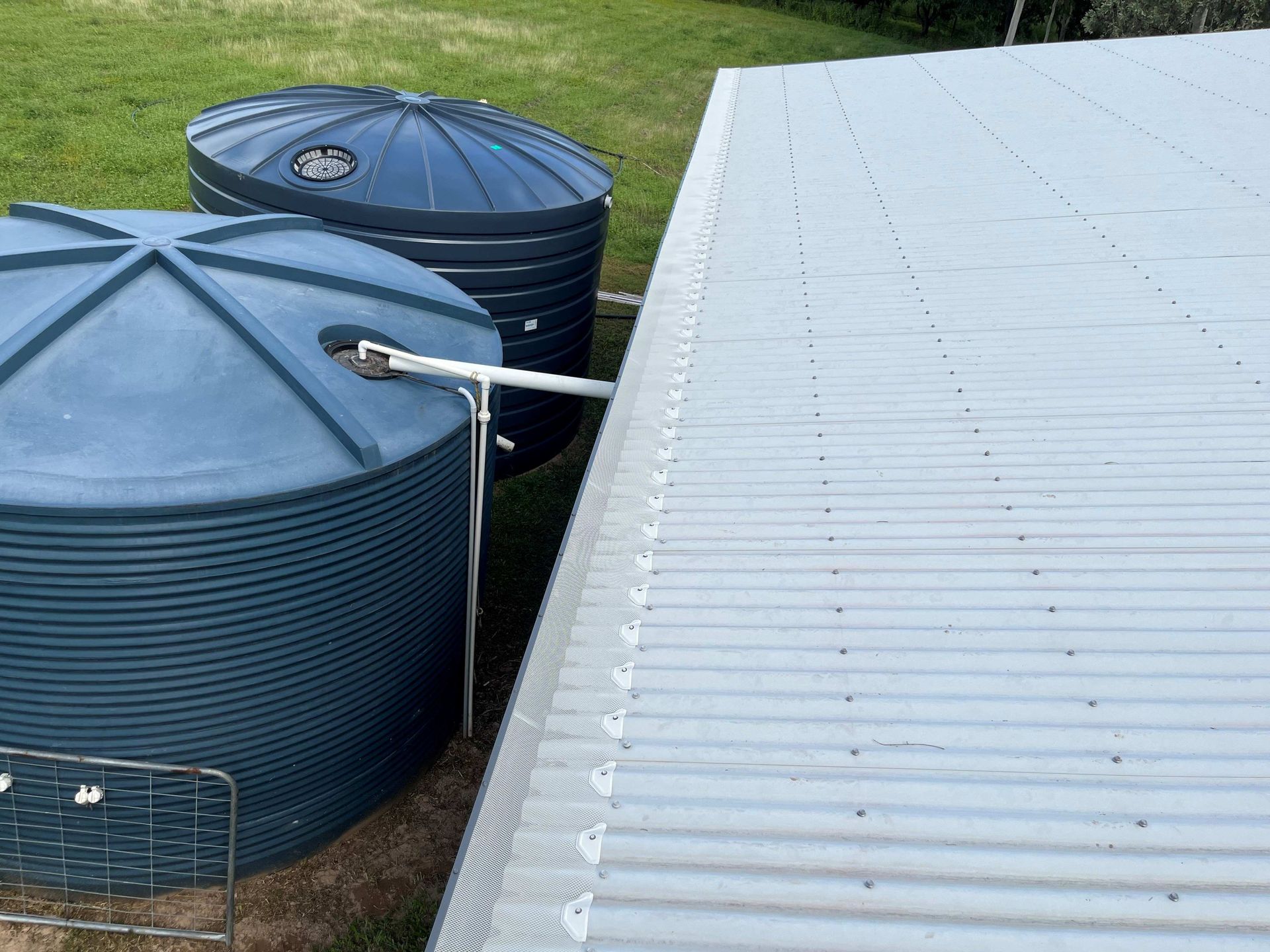 Two Blue Water Tanks Next to A Light Gray Corrugated Metal Roof with A Gutter — All-Clear Gutter Guard NQ in Mission Beach, QLD