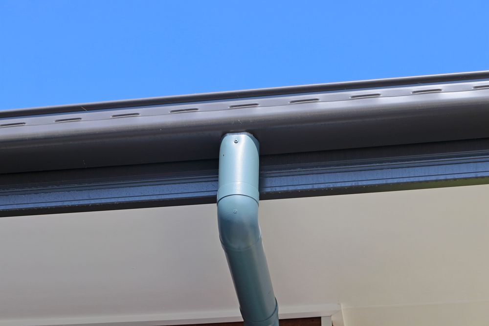 Gray rain gutter and downspout on a white house, against a blue sky — All-Clear Gutter Guard NQ in Cairns City, QLD