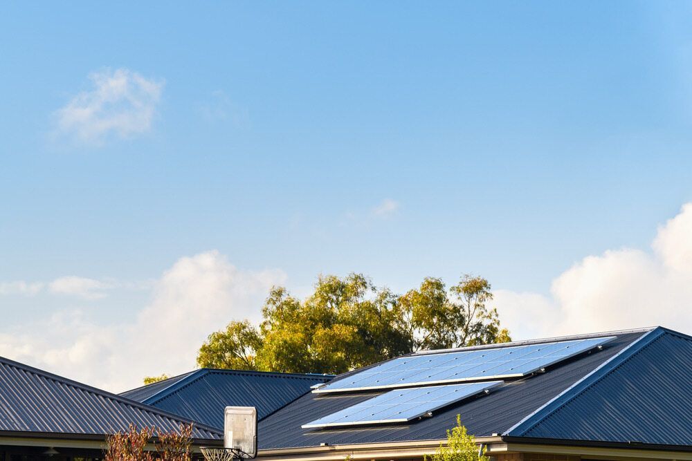 Blue Solar Panels on A Dark Roof Under a Bright Blue Sky with A Few Clouds — All-Clear Gutter Guard NQ in Innisfail, QLD