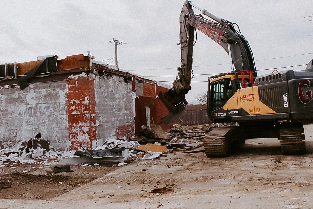 A large excavator is demolishing a building in a dirt field.