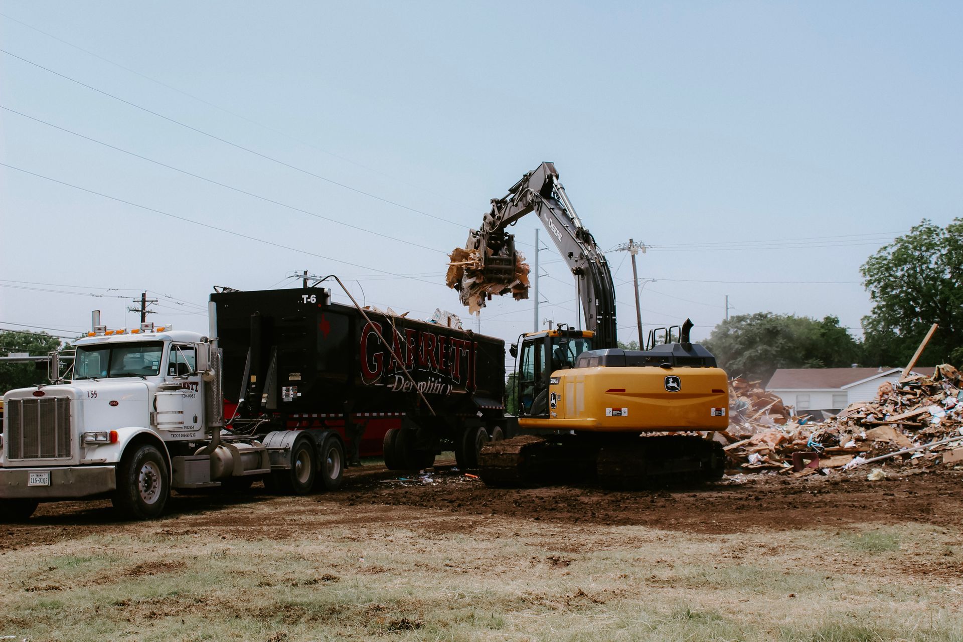 A truck is being loaded with a dumpster by a bulldozer.