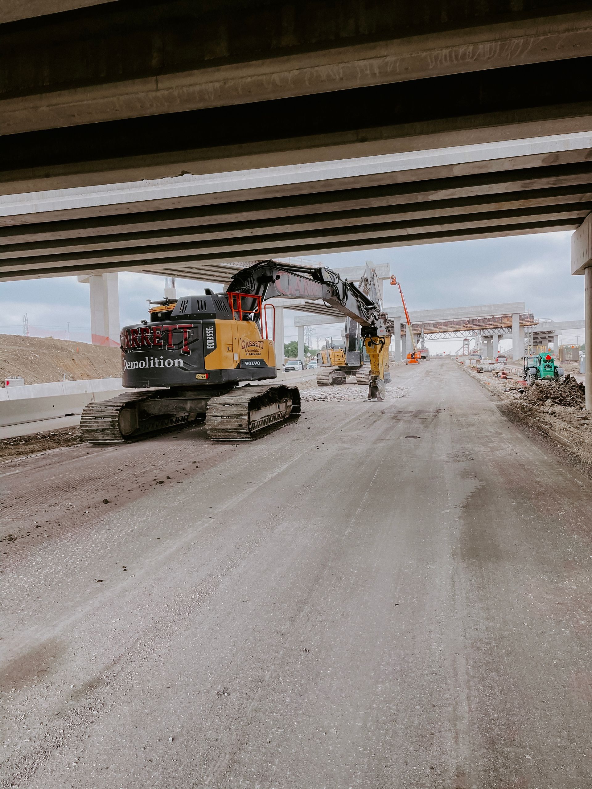 A construction vehicle is driving down a road under a bridge.