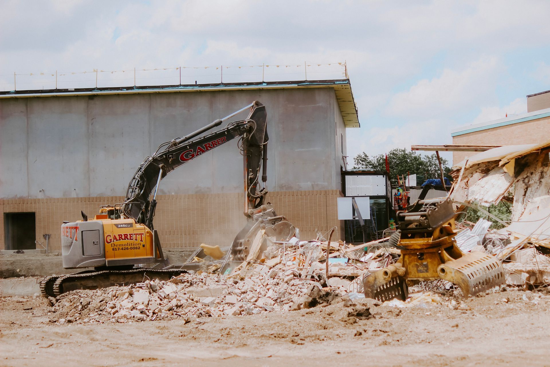 A yellow excavator is demolishing a building on a construction site.