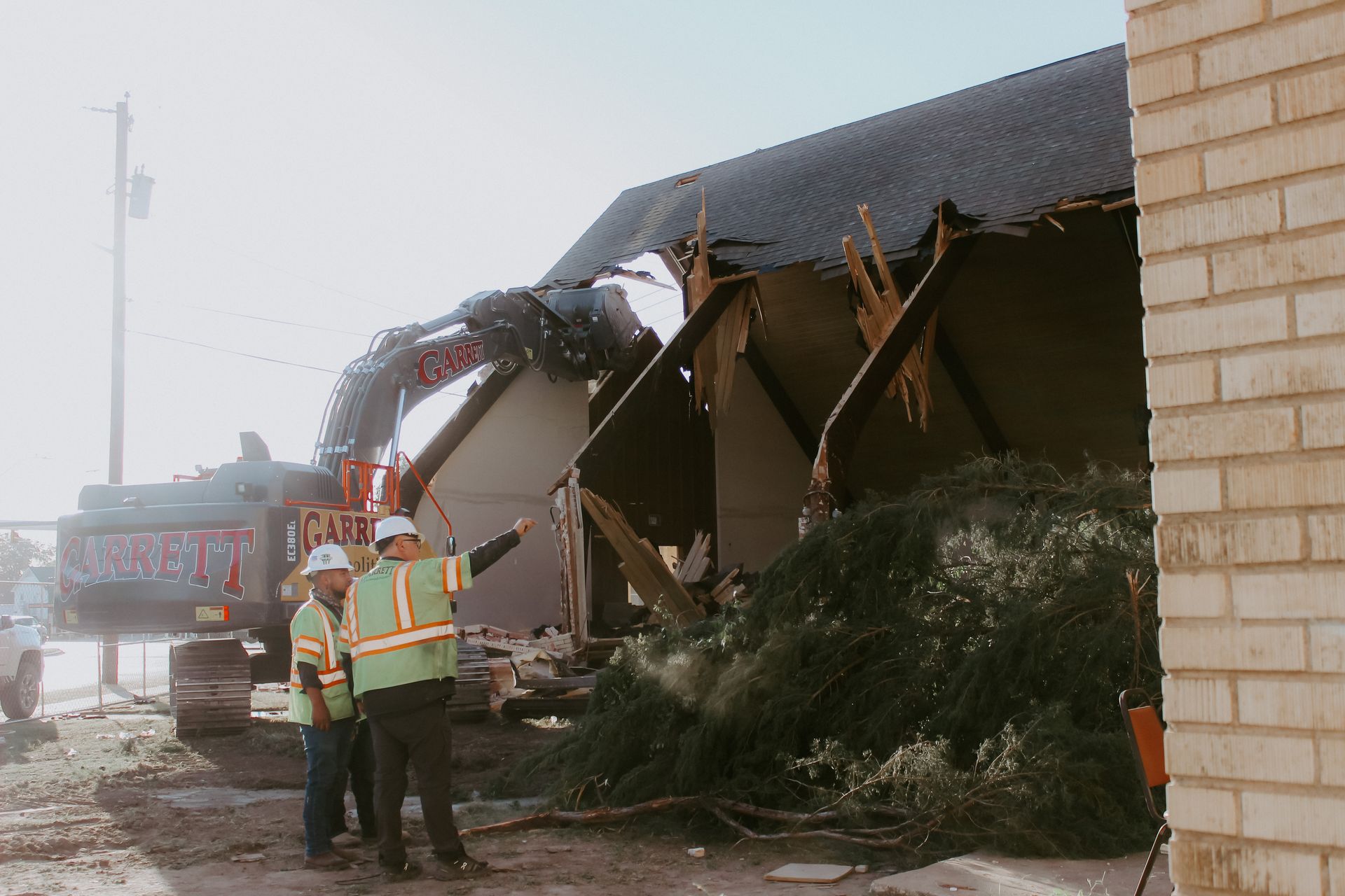 Two construction workers are standing in front of a building that is being demolished.