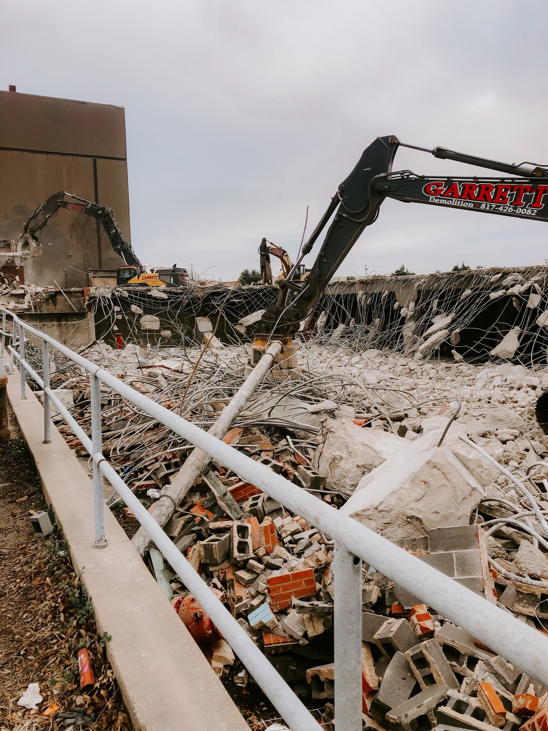 A demolition site with a white railing and a large excavator.