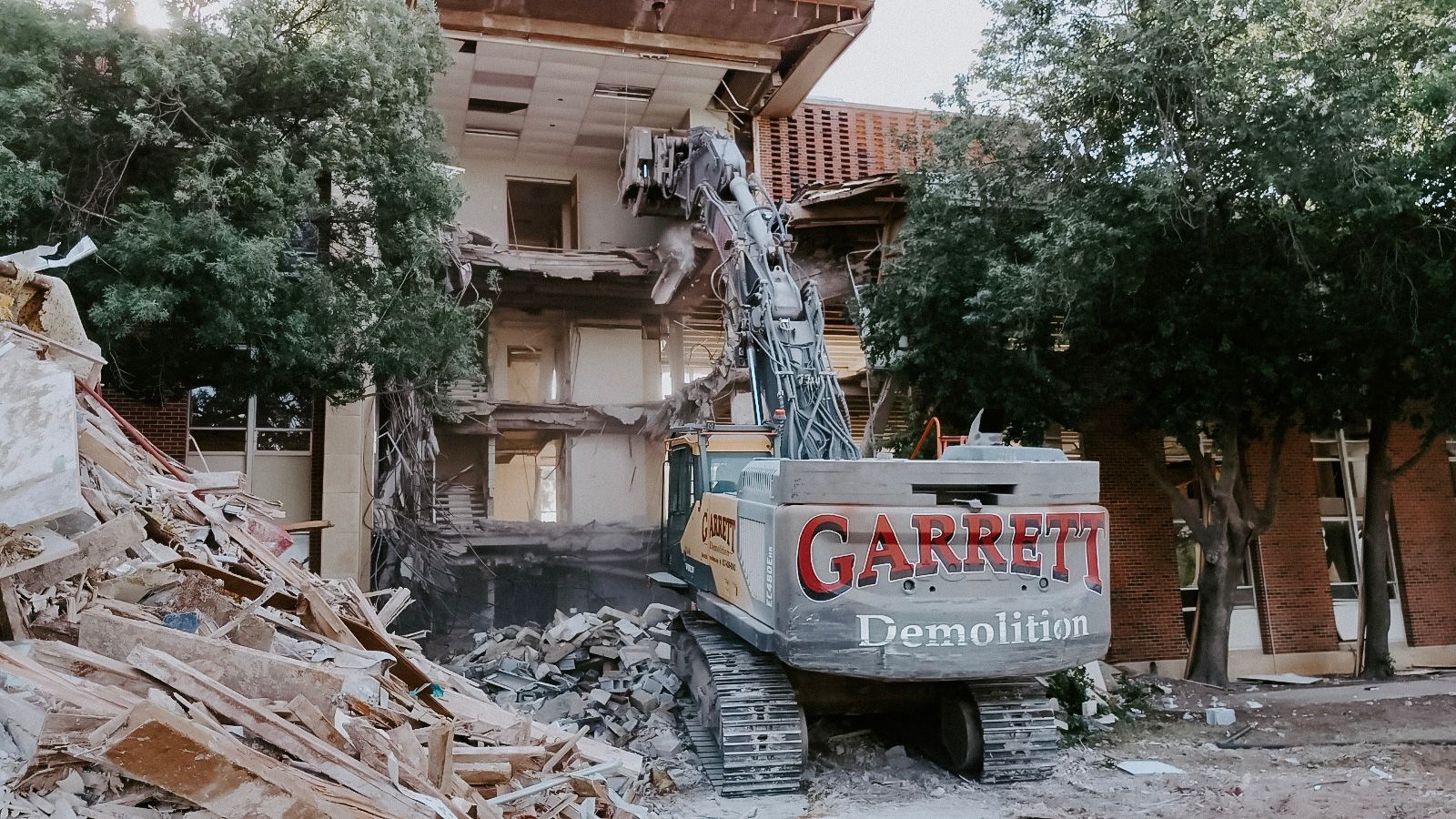 A large building is being demolished by a garrett excavator.