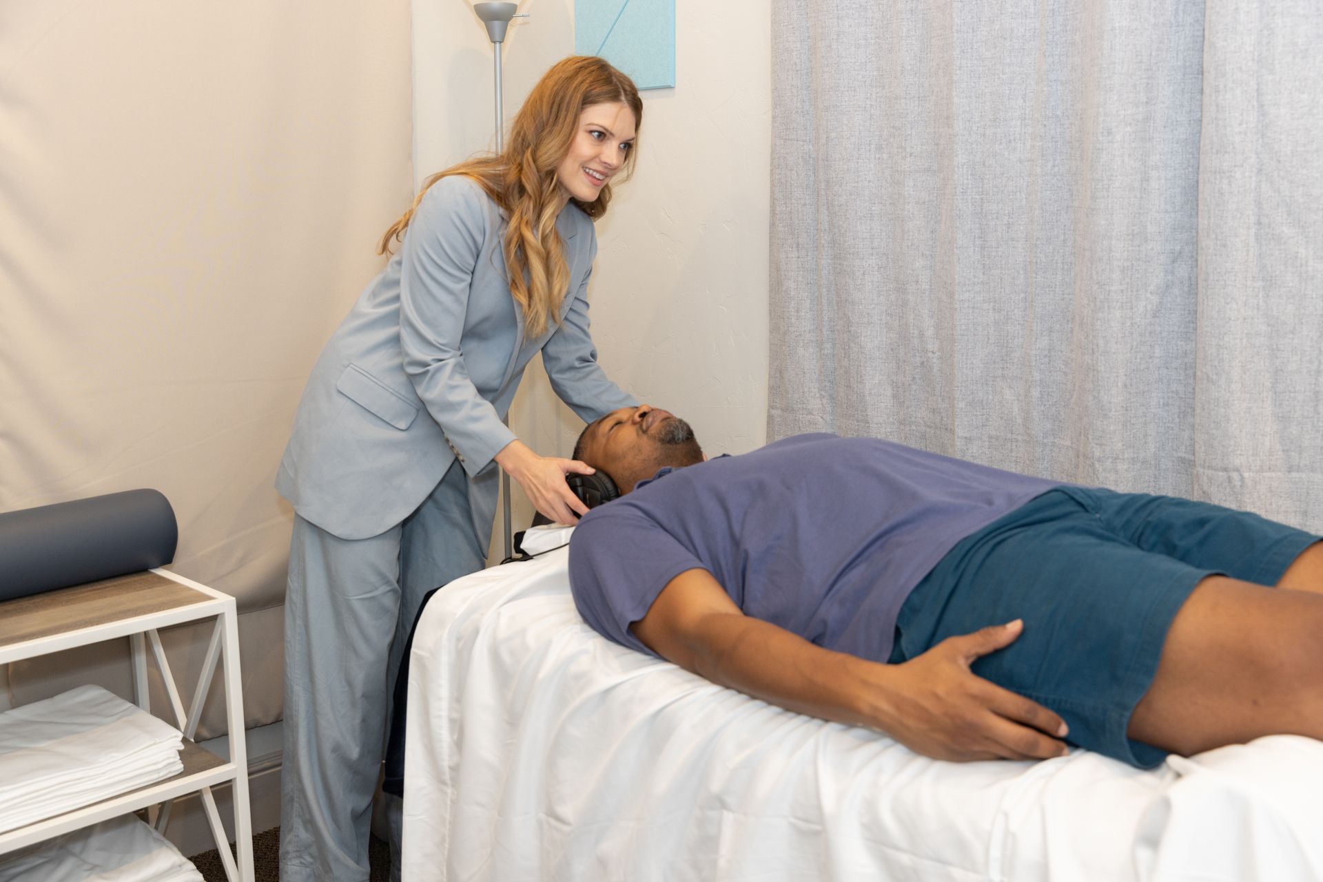 woman putting headphones on a man laying on a vibroacoustic sound therapy bed for anxiety healing