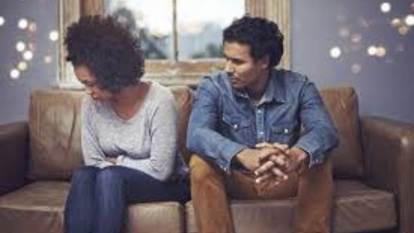 Woman with crossed arms and man sitting on a sofa, looking at each other, appearing to be in conflict and going to couples counseling grapevine texas.