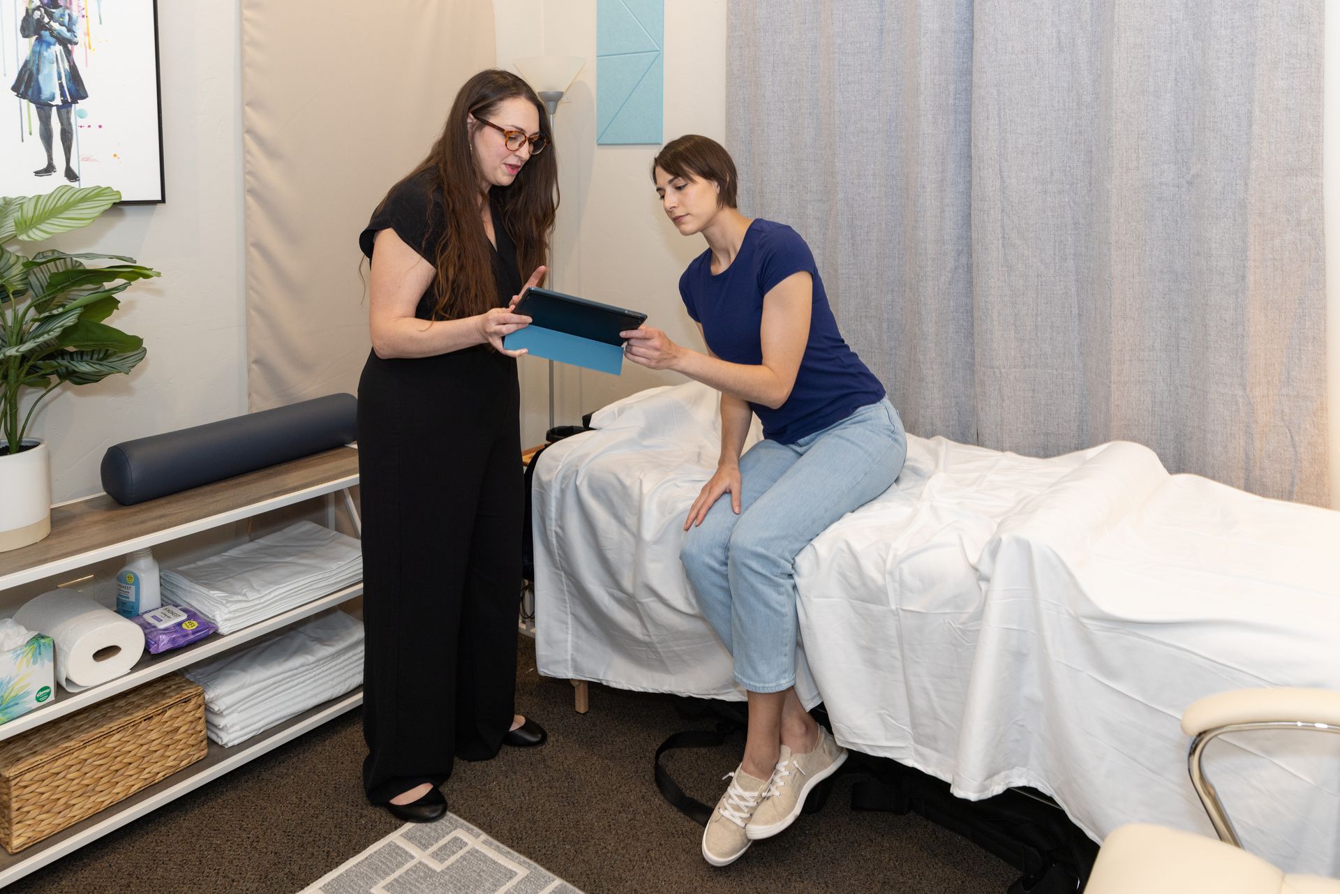 A woman is sitting on a bed talking to another woman, choosing healing sound frequency for Vibroacoustic Sound healing.