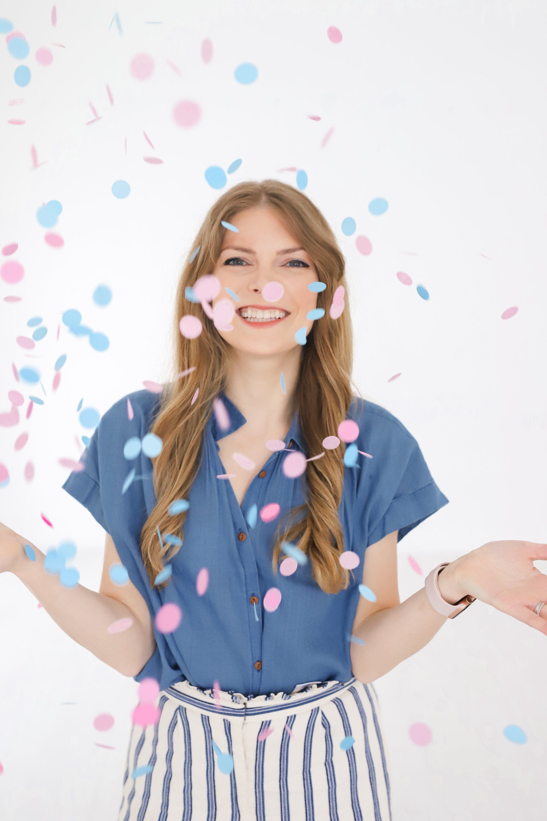 A woman is standing in front of a wall with confetti falling around her.