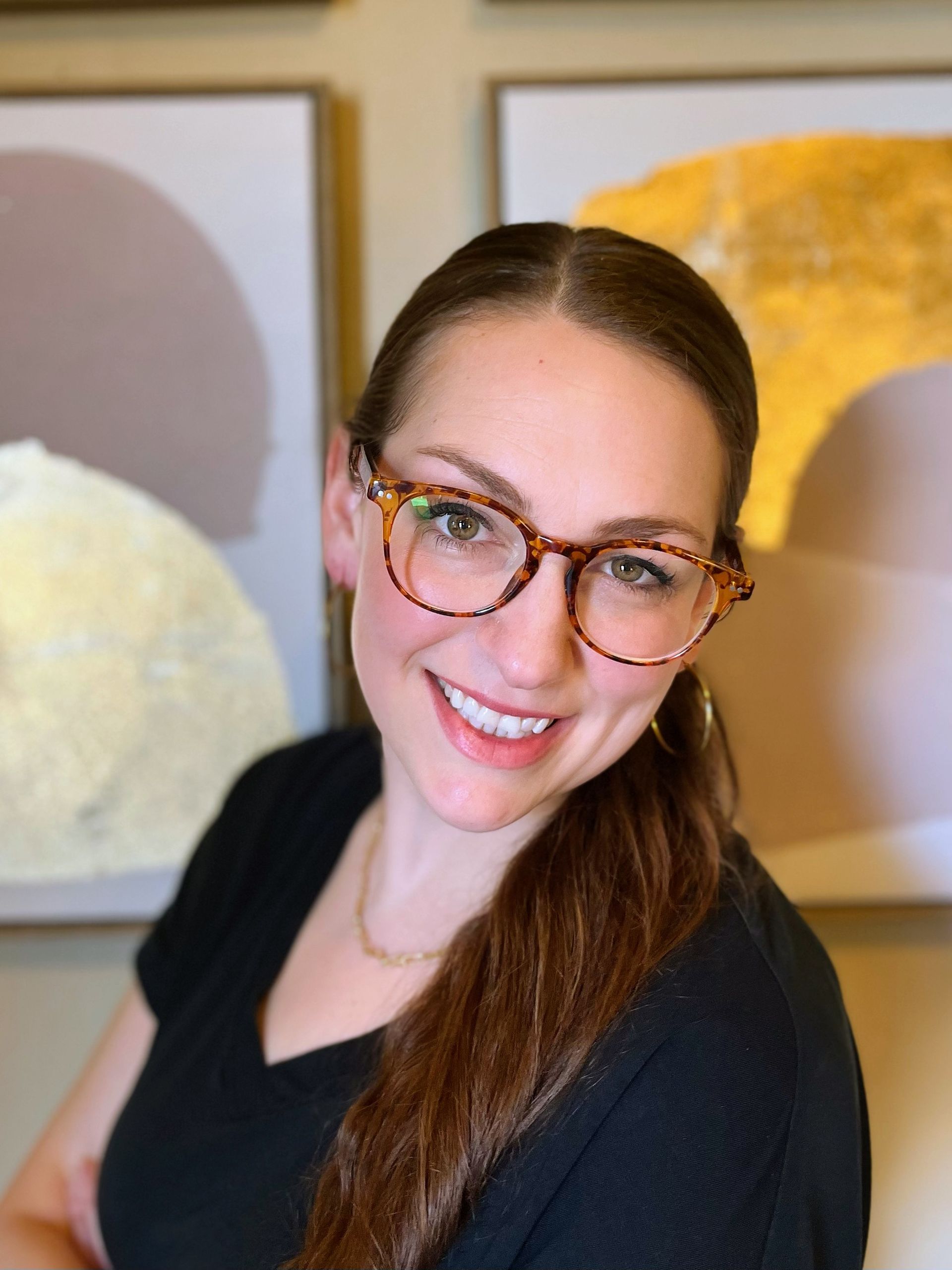 A woman wearing glasses and a black shirt is smiling for the camera a postpartum counselor in Texas.