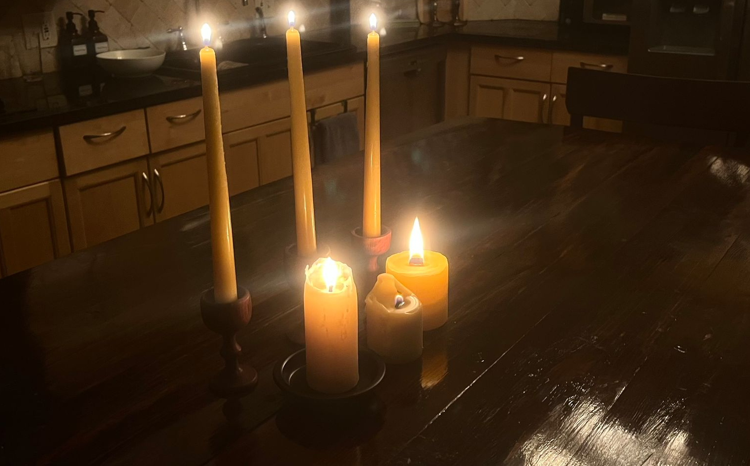 Lit candles on a dark wooden table in a dimly lit kitchen for seasonal living in texas.