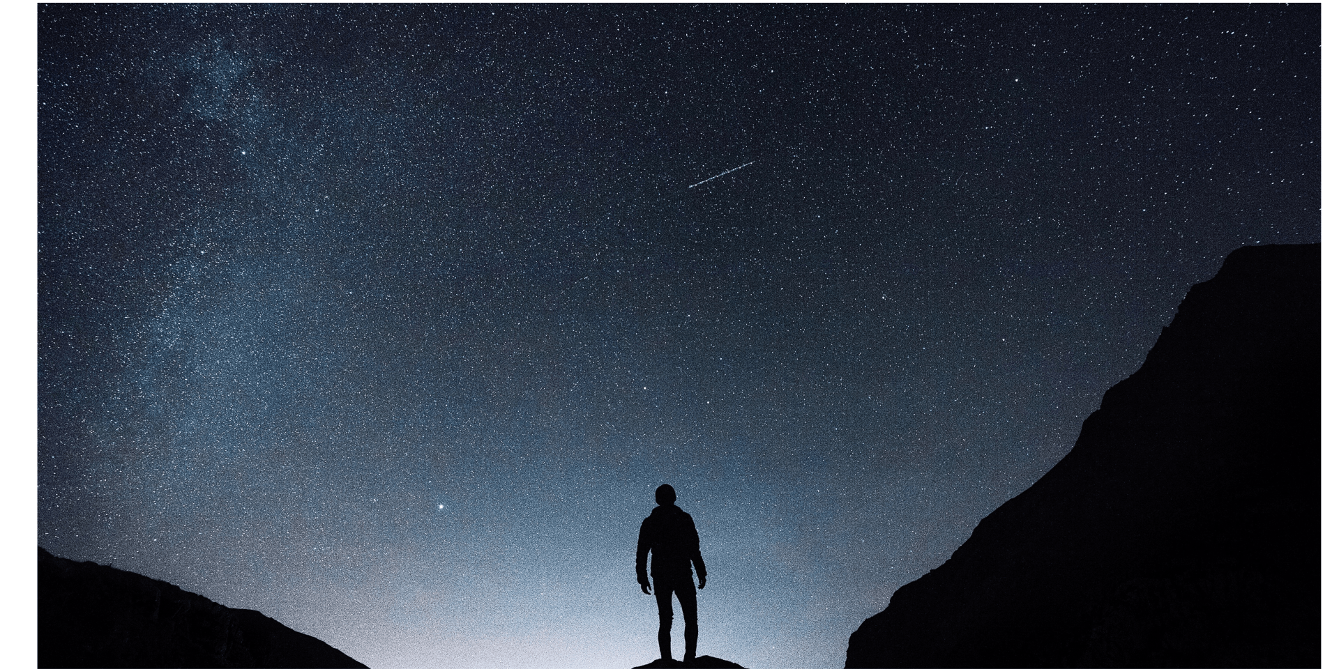 A man is standing on top of a mountain under a starry night sky.