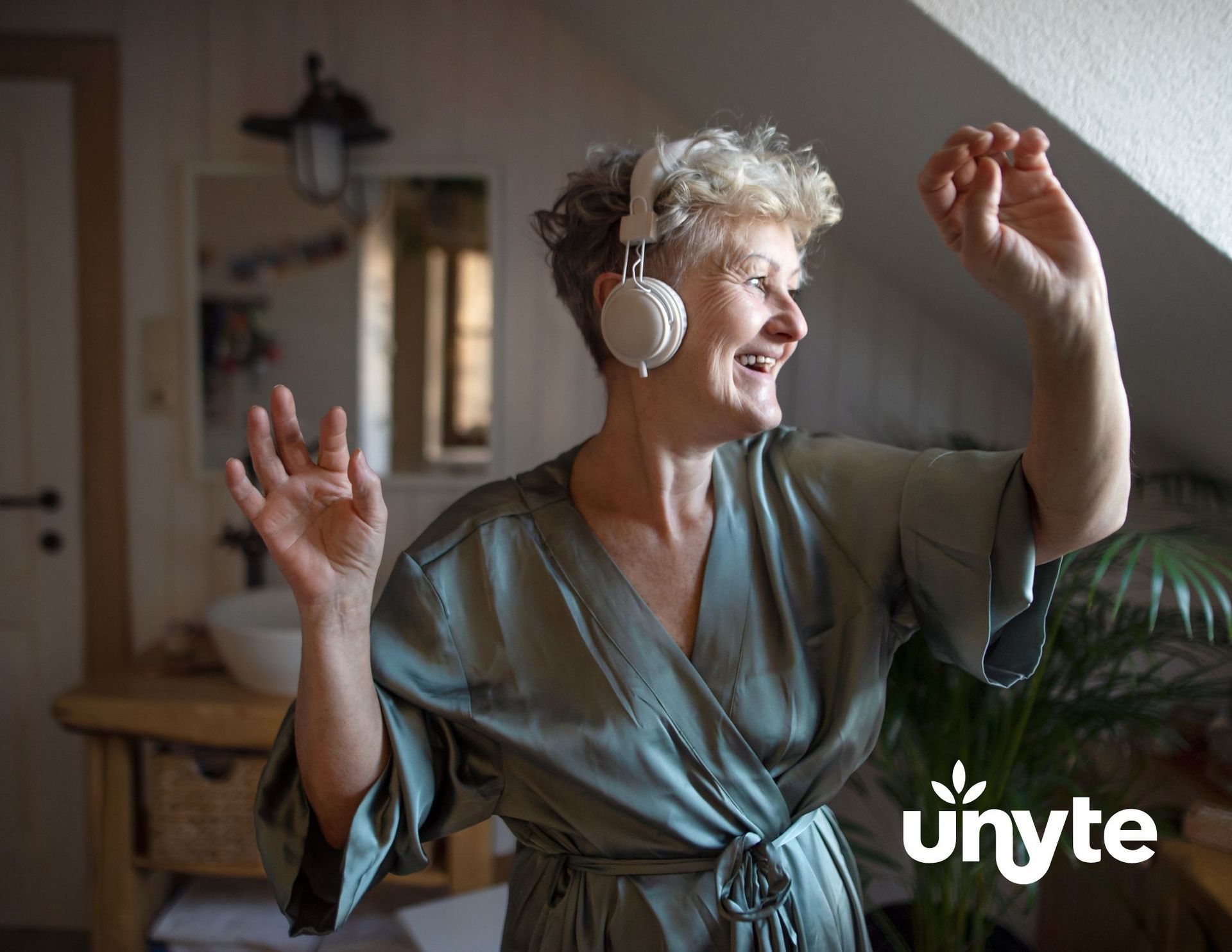An elderly woman wearing headphones is dancing in a room listening to SSP