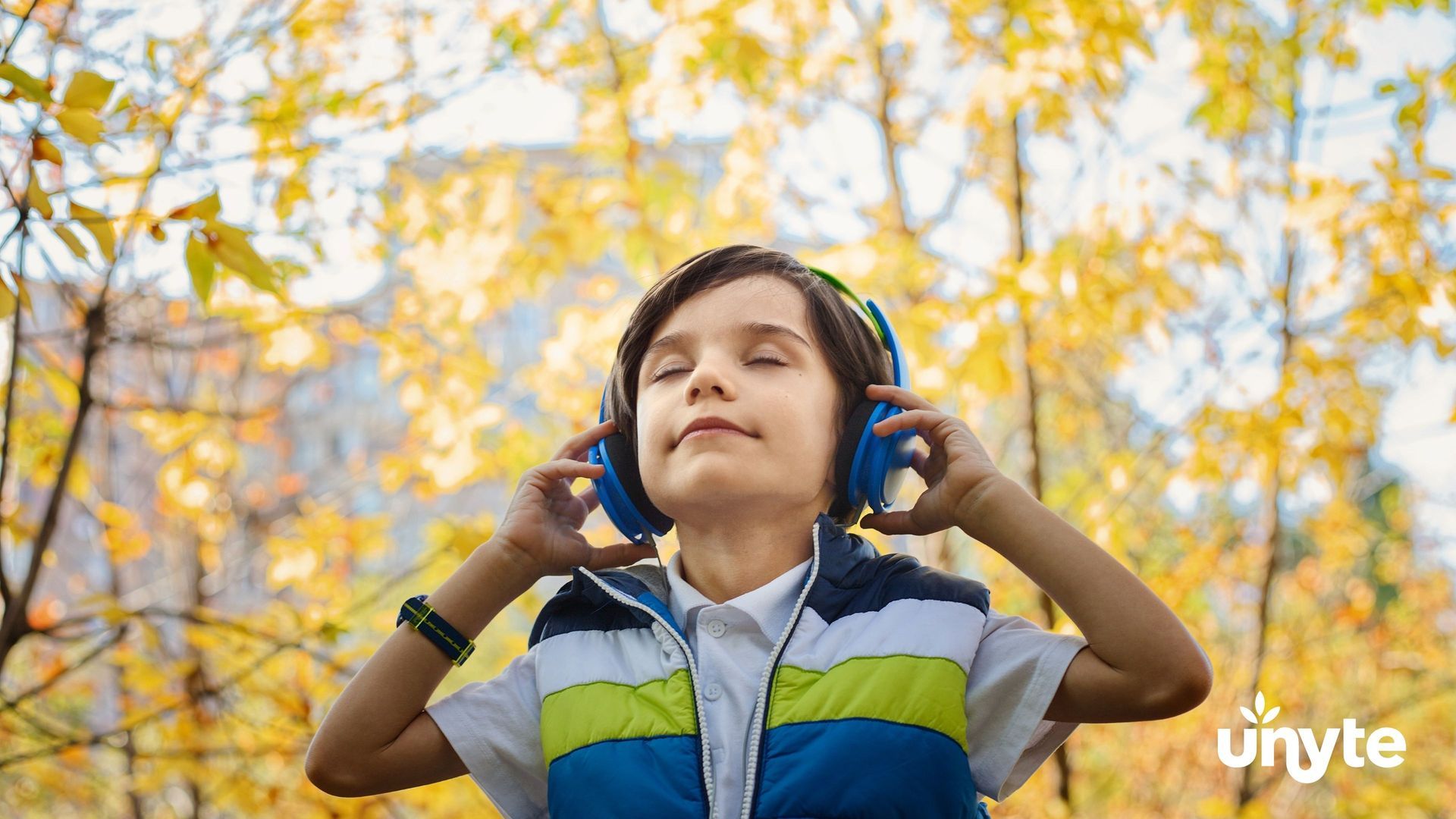 Child wearing blue headphones listening to RRP outdoors among yellow autumn leaves
