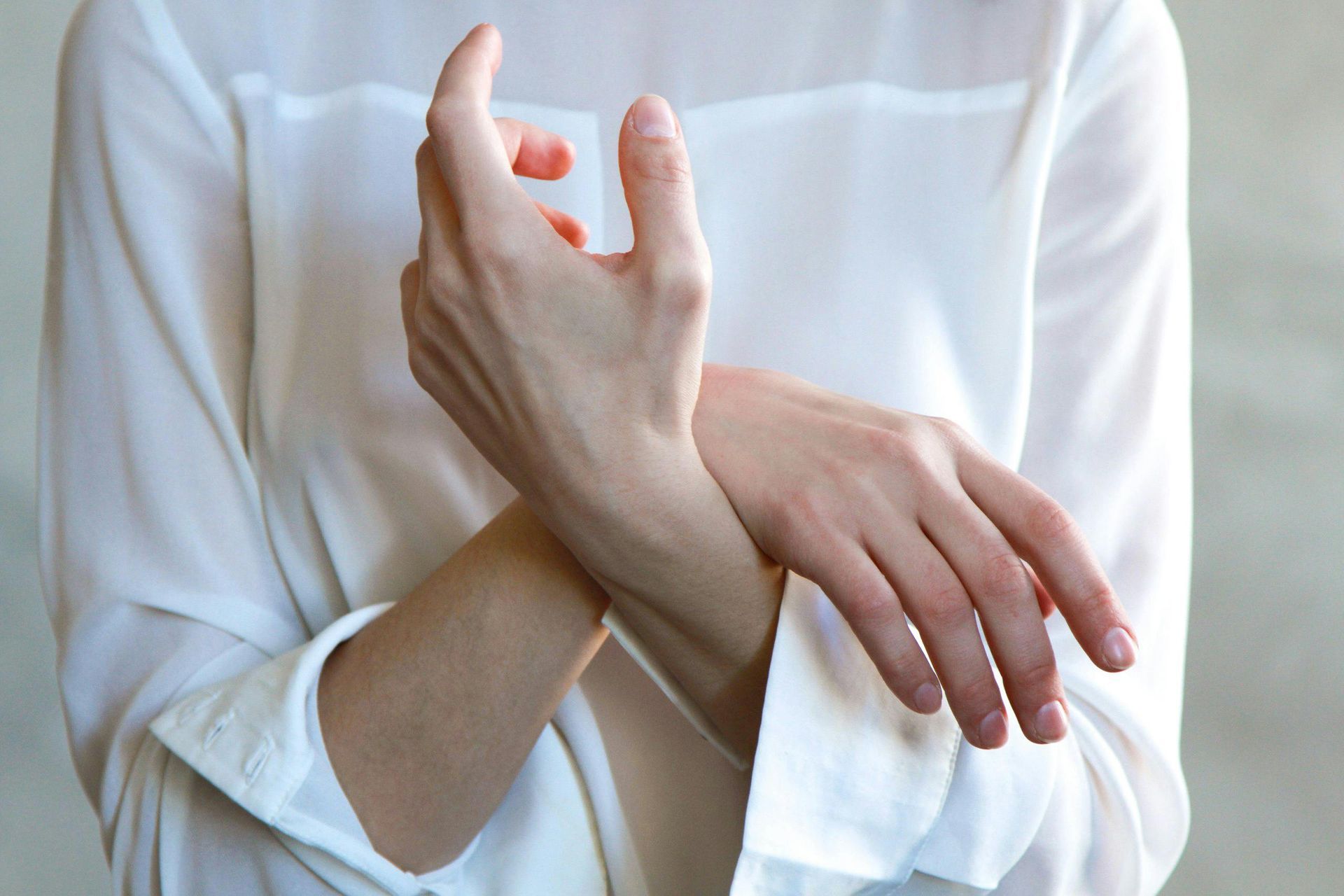 A woman in a white shirt is holding her wrist due to chronic pain and is using muscle relaxation. 