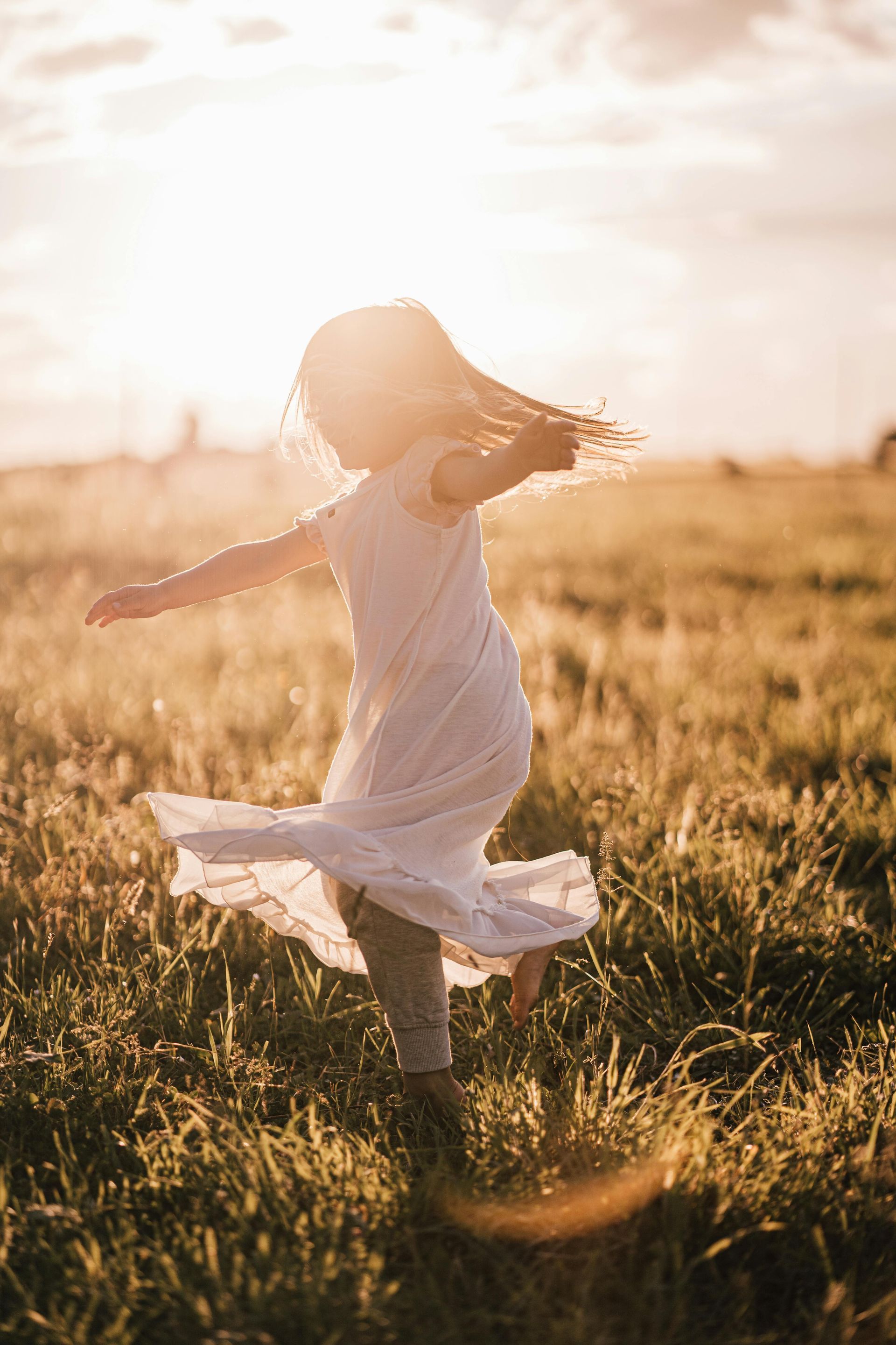 A little girl in a white dress is running in a field at sunset.