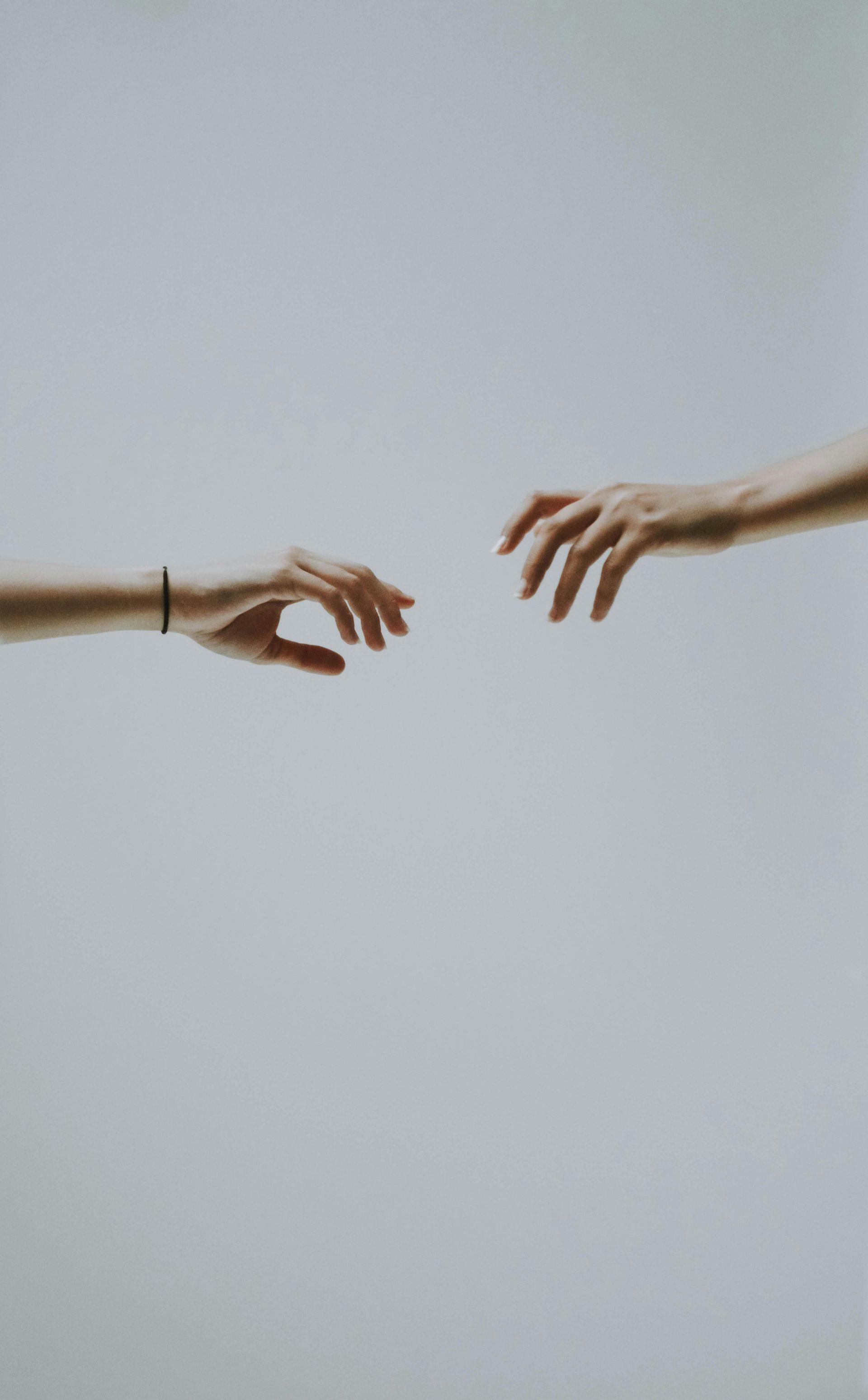 Two arms outstretched, hands almost touching, set against a neutral gray background.