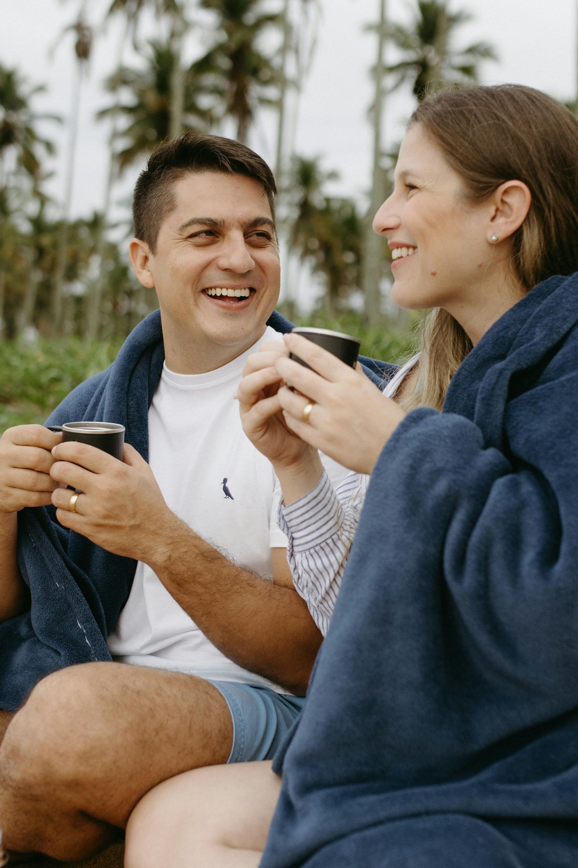 A man and a woman are sitting under a blanket holding cups of coffee. Couple celebrating the holidays 