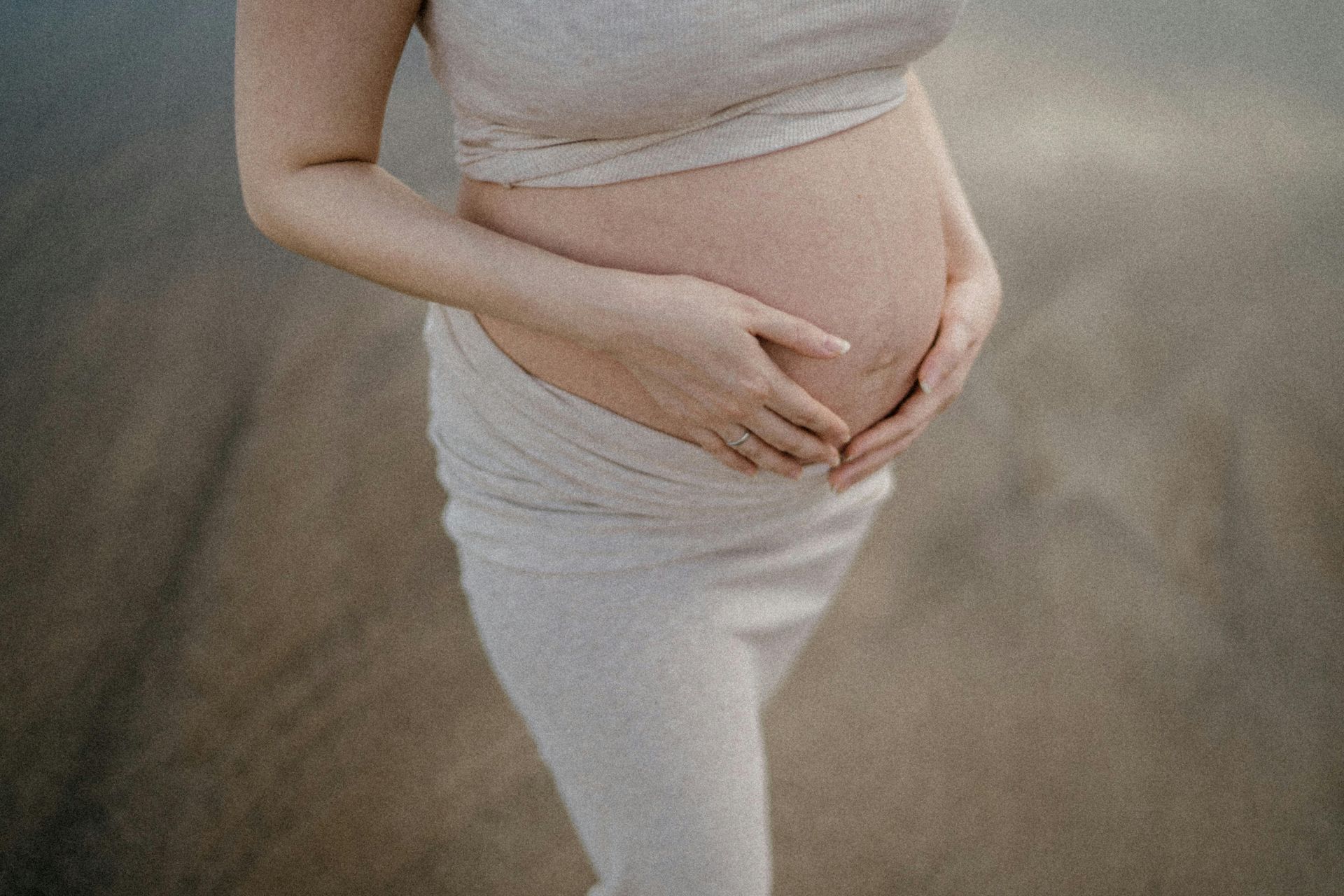A pregnant woman is holding her belly on the beach receiving maternal counseling in DFW.