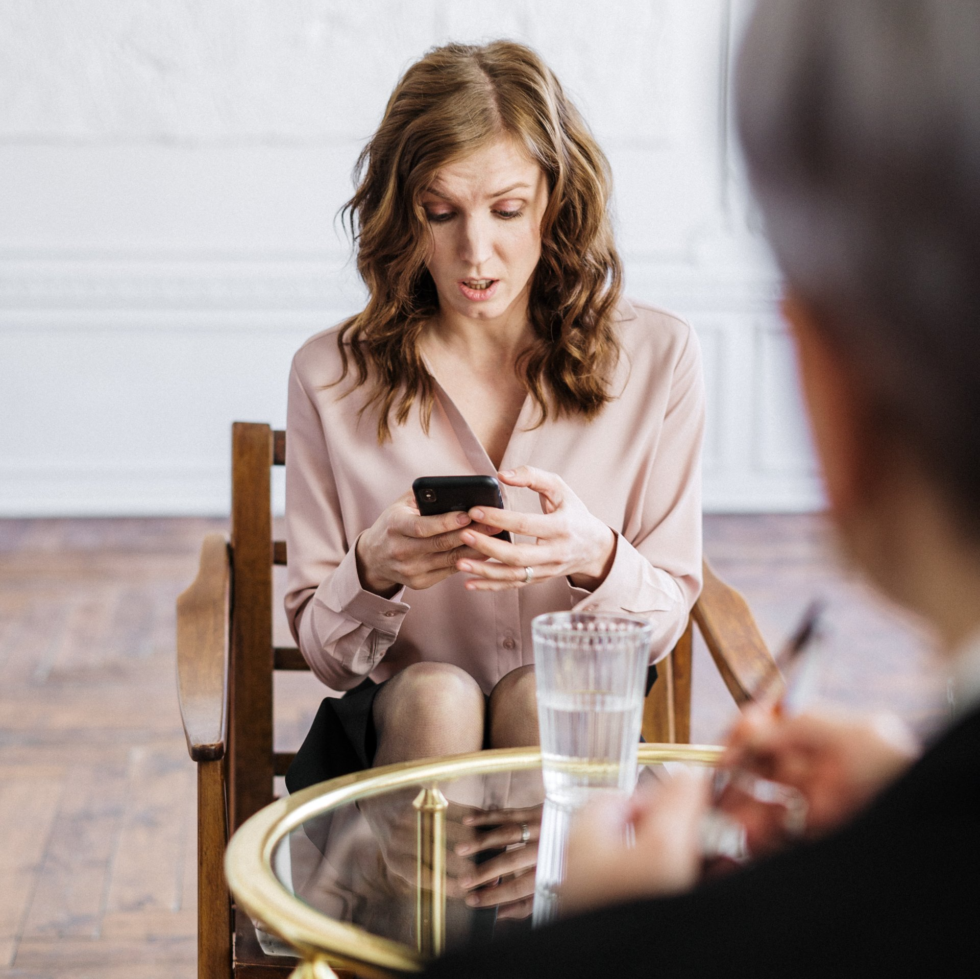 a woman is sitting at a table looking at her phone to schedule a somatic therapy counseling session in Grapevine Texas.